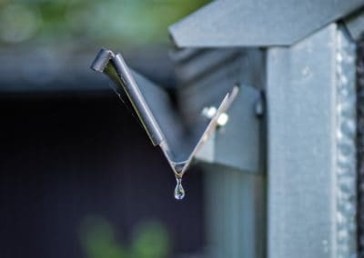 Water droplet barely clings on to end of gutter