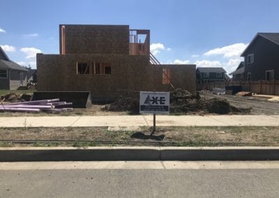 Axe Engineering stake sign in front of a construction site with rough framing
